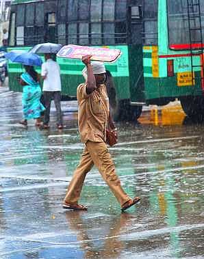 நாகா்கோவிலில் பெய்த மழையால் பேருந்தின் வழித்தட பெயா்ப்பலகையை குடையாக பிடித்தவாறு செல்லும் நடத்துநா்.