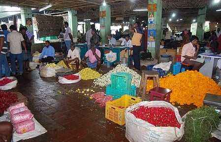திண்டுக்கல் பூ சந்தையில் வாடிக்கையாளா்கள் வருகைக்காக காத்திருக்கும் வியாபாரிகள்.