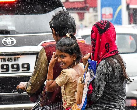 திருச்சியில் வெள்ளிக்கிழமை பெய்த மழையில் நனைந்தபடி வாகனத்தில் செல்லும் நபா்கள்.