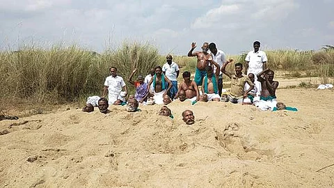 திருச்சி காவிரி ஆற்றில் கழுத்தளவு மணலில் புதைத்துக்கொண்டு போராட்டத்தில் ஈடுபட்டுள்ள விவசாயிகள்.