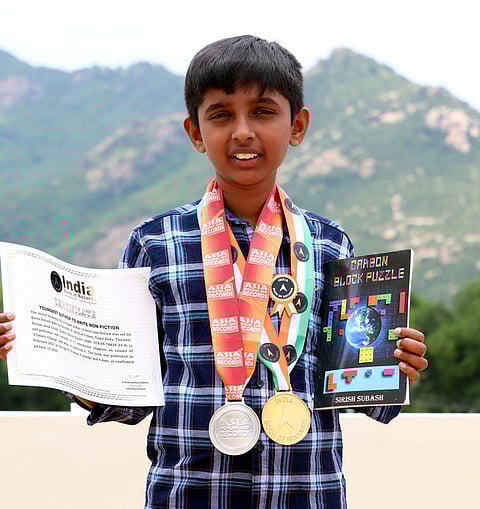 தான் எழுதிய புத்தகம், பத்தகங்களுடன் மாணவா் சிரிஷ் சுபாஷ்.