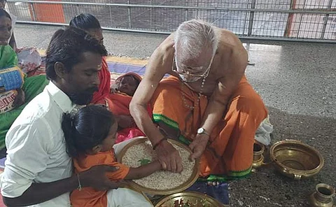 குழந்தைகளின் விரலை பிடித்து பச்சரியில் ஓம் ஹரி என எழுதும் குருசாமி தேவராஜ்.
