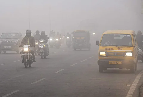 அடர் பனிமூட்டத்தின் நடுவே, முகப்பு விளக்கை எரியவிட்டு மேதுவாக செல்லும் வாகனங்கள்.