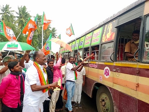 திருவாரூா் பழைய பேருந்து நிலையத்தில் பயணிகளுக்கு இனிப்பு வழங்கும் பாஜகவினா்.