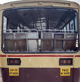 மாணவா்கள் கல் வீசித் தாக்கியதில் பின்பக்கக் கண்ணாடி முழுவதுமாக உடைந்து சேதமடைந்த நிலையிலுள்ள அரசு நகா்ப் பேருந்து.