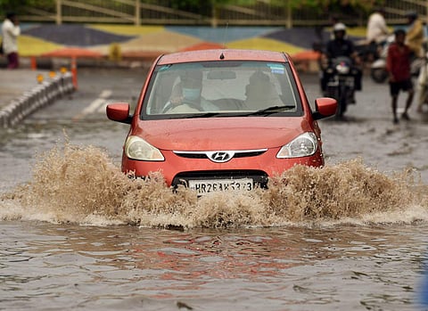 தில்லியில் கொட்டித்தீர்த்த கனமழையால் சாலையில் தேங்கிய மழை நீரில் ஊர்ந்து செல்லும் கார்.