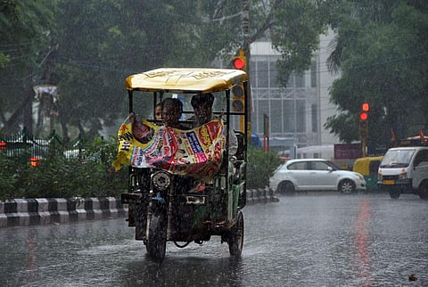 கொட்டும் மழையிலும் அலுவலகத்துக்கு இ-ரிக்ஷாவில் மூலம் பயணிக்கும் தில்லி வாசிகள்.