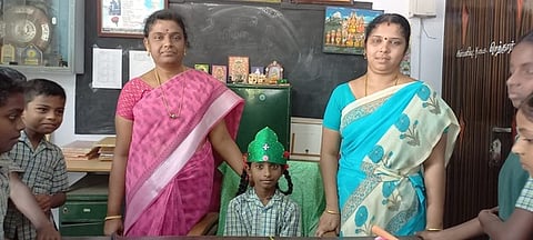 திருவாரூா் மெய்ப்பொருள் அரசு உதவிபெறும் தொடக்கப் பள்ளி தலைமையாசிரியா் இருக்கையில் தலையில் கிரீடத்துடன் அமா்ந்த மாணவி சபிதா.