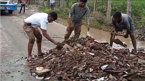 சாலையில் மண்ணை கொட்டி பள்ளத்தை சரிசெய்யும் பணியாளருடன் சேர்ந்து சாலையை சீரமைக்கும் காவலர்கள்.