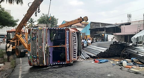 சாலையில் நடுவில் இரும்புக் குழாய்களுடன் கவிழ்ந்து கிடக்கும் லாரி.