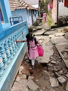 வால்பாறை சிறுவா் பூங்கா குடியிருப்பு பகுதியில்  பழுதடைந்த நடைபாதை வழியாக தடுமாறி செல்லும் பள்ளி மாணவி .
