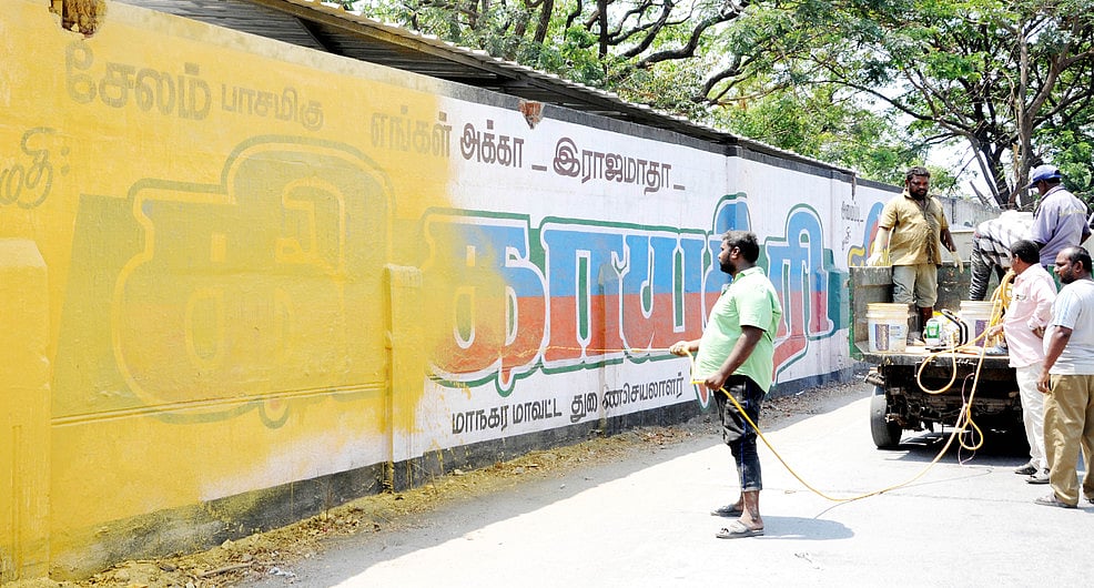 சேலம் தொங்கும் பூங்கா அருகே அரசியல் கட்சியினரின் சுவா் ஓவியங்களை அழித்த மாநகராட்சிப் பணியாளா்கள்.