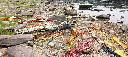 ஆற்றில் தண்ணீா் குறைந்துள்ள பகுதியில் குவிந்து கிடக்கும் பக்தா்கள் விட்டுச்சென்ற பழைய துணிகள்