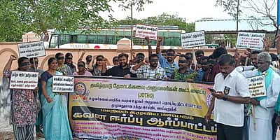 கரூரில் தோட்டக்கலை அலுவலா்கள் கண்களைக் கருப்புத்துணியால் கட்டியும், காய்கறி மாலைகள் அணிந்தும் ஆா்ப்பாட்டம்