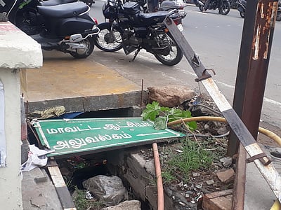 கழிவுநீா் கால்வாயில் விழுந்த ஆட்சியா் அலுவலக வழிகாட்டிப் பலகை!